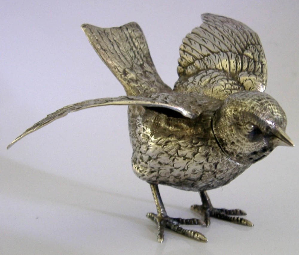 A solid silver pepper pot finely chased in the detailed form of a bird chick with outstretched wings.