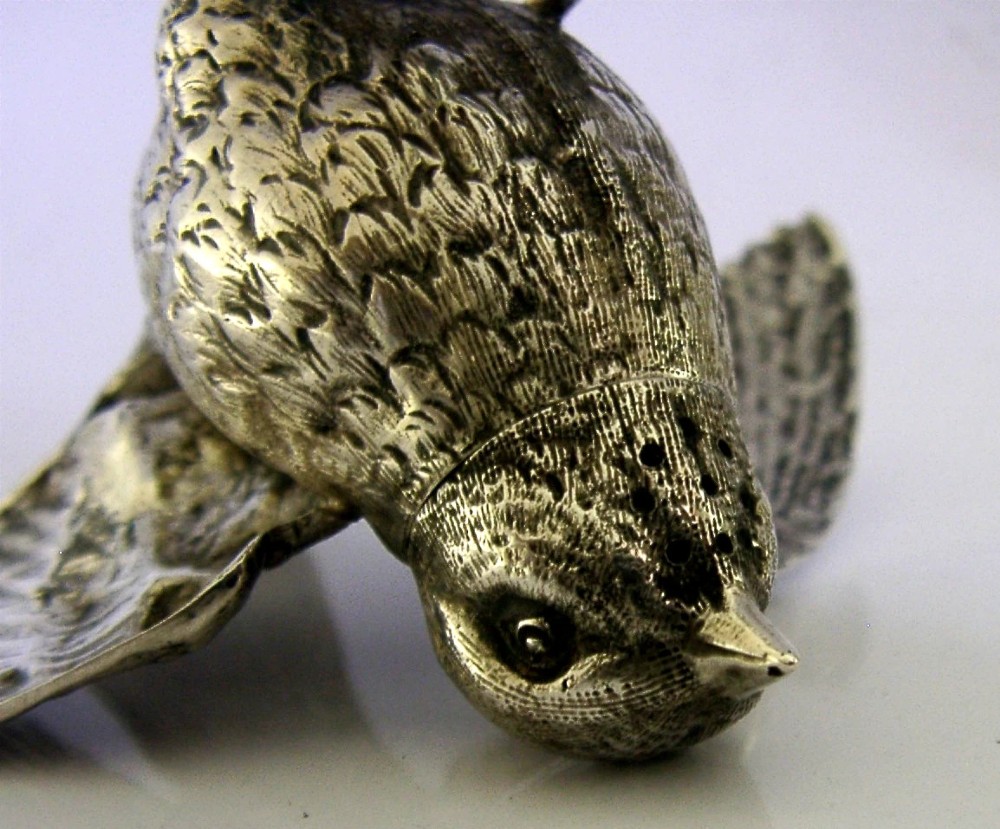 A solid silver pepper pot finely chased in the detailed form of a bird chick with outstretched wings. View X