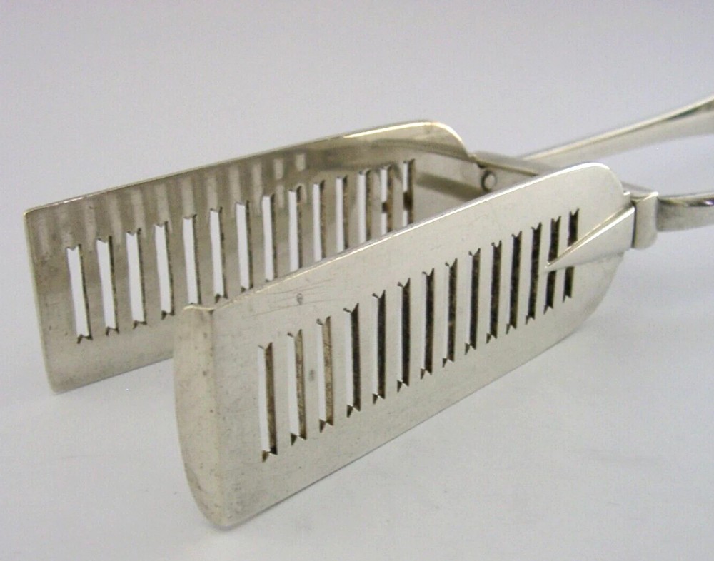 Victorian sterling silver serving tongs featuring slotted rectangular blades and a spring-hinged handle stamped with hallmarks. View V