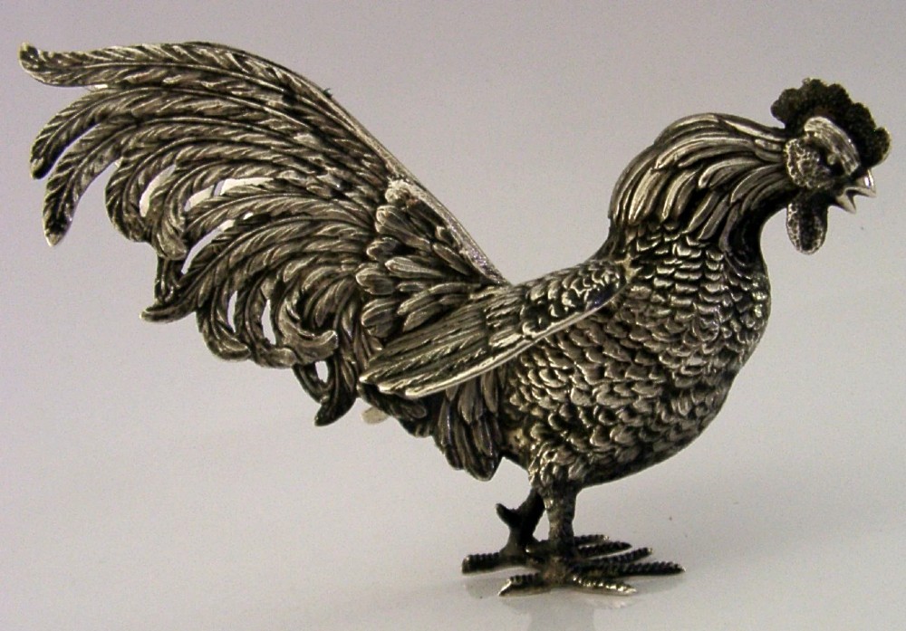 A solid silver figurine of a cockerel standing with open tail feathers and detailed feather chasing.