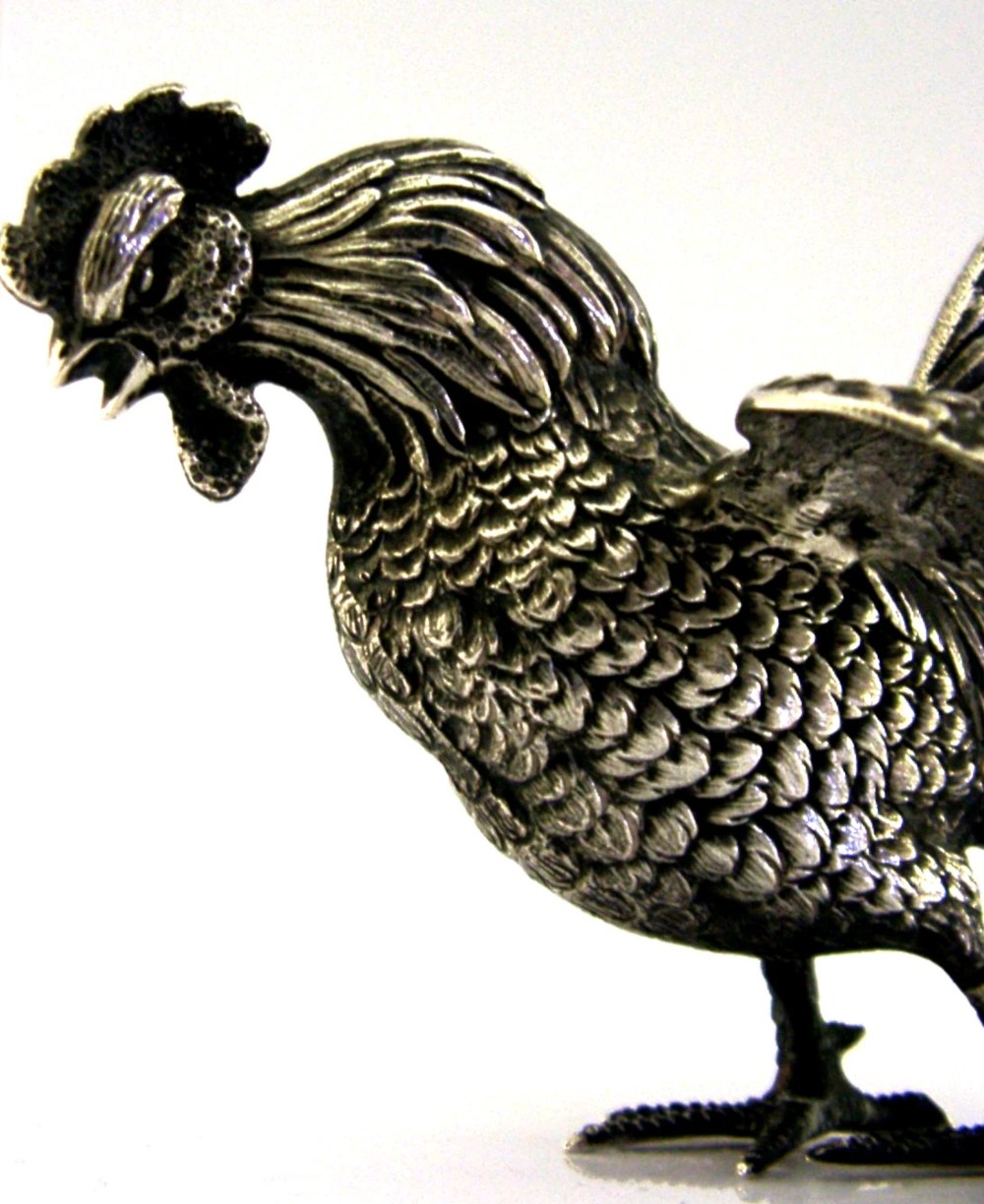 A solid silver figurine of a cockerel standing with open tail feathers and detailed feather chasing. View II