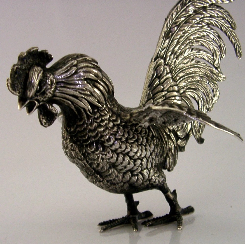 A solid silver figurine of a cockerel standing with open tail feathers and detailed feather chasing. View III