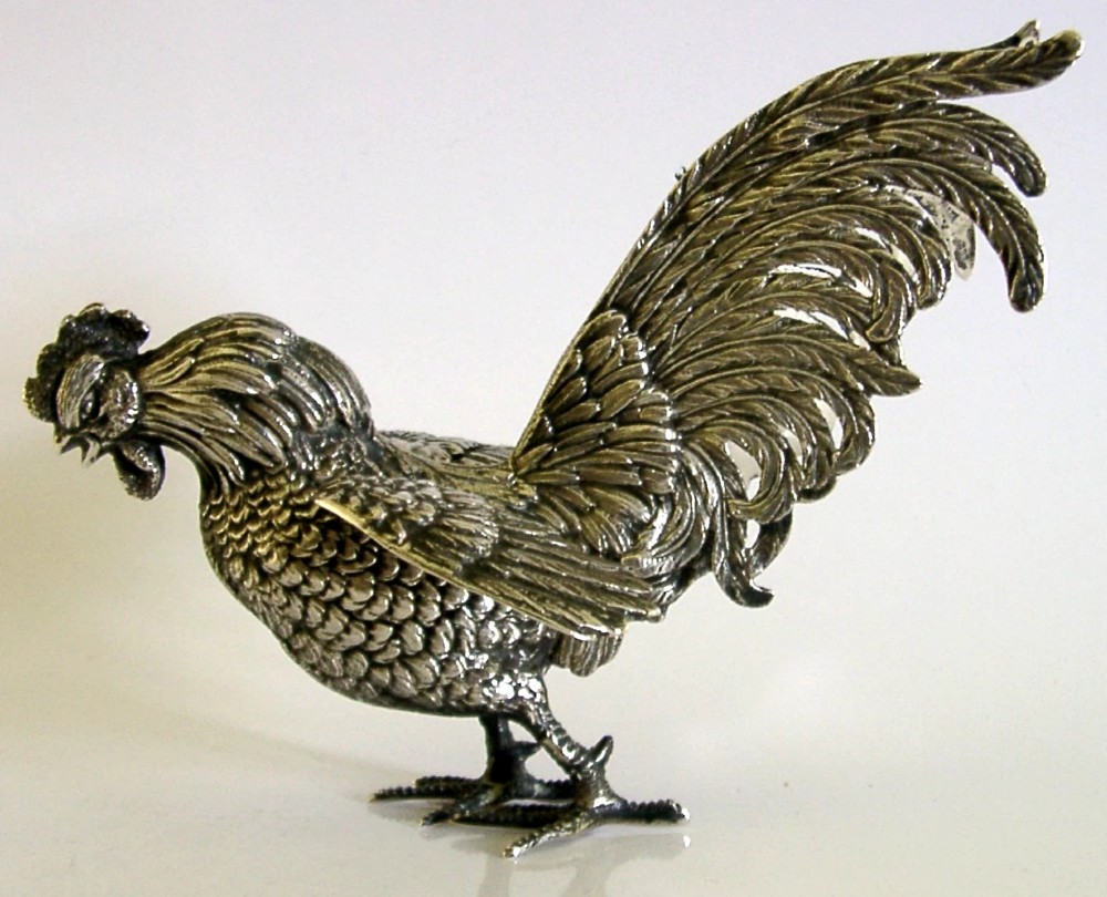 A solid silver figurine of a cockerel standing with open tail feathers and detailed feather chasing. View IV