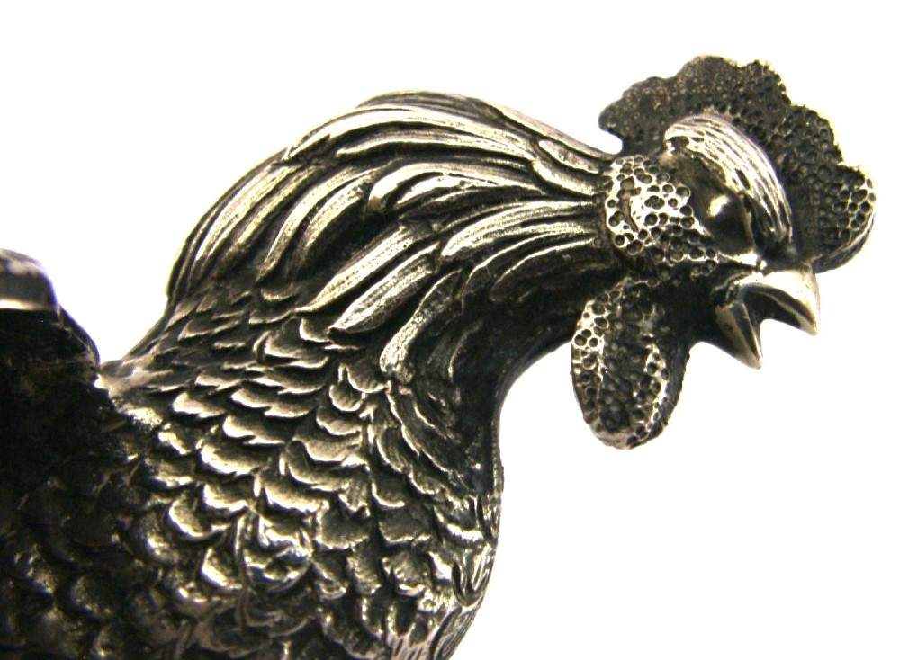 A solid silver figurine of a cockerel standing with open tail feathers and detailed feather chasing. View V