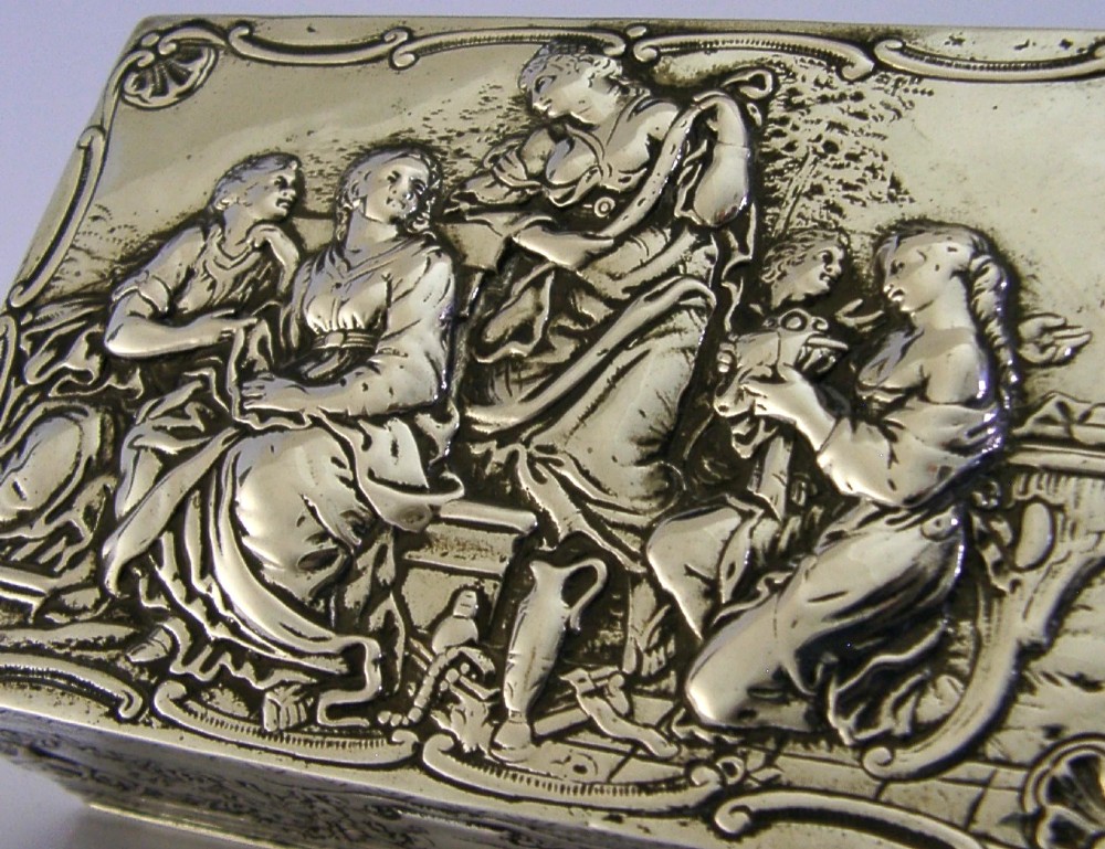 A rectangular silver box featuring embossed classical figures on the hinged lid and foliate scrollwork along the sides. View II