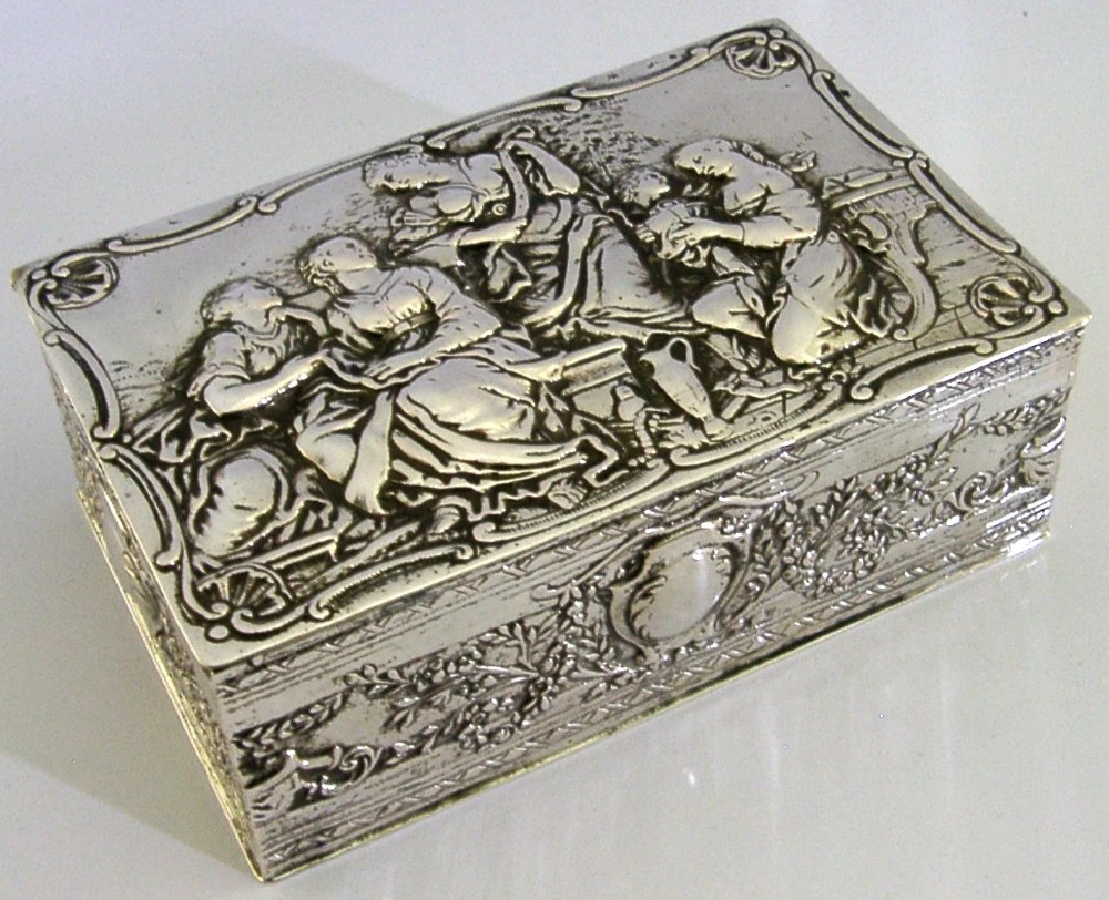 A rectangular silver box featuring embossed classical figures on the hinged lid and foliate scrollwork along the sides. View III