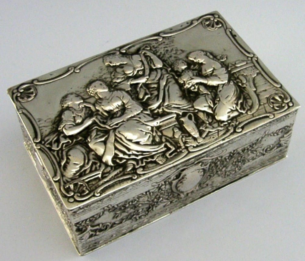 A rectangular silver box featuring embossed classical figures on the hinged lid and foliate scrollwork along the sides. View IV