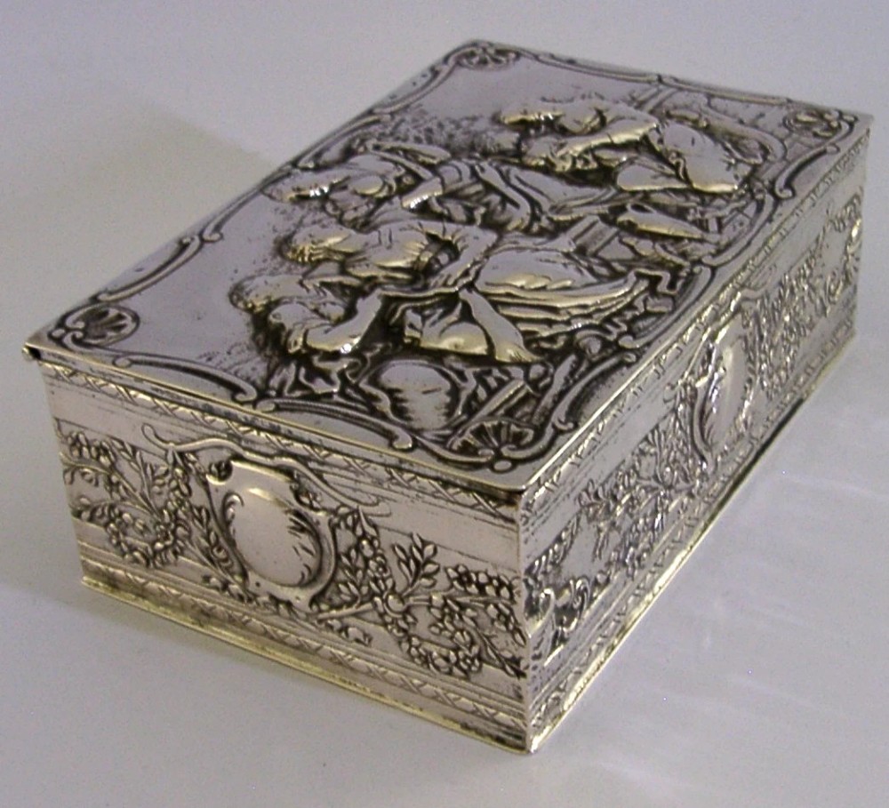 A rectangular silver box featuring embossed classical figures on the hinged lid and foliate scrollwork along the sides. View IX