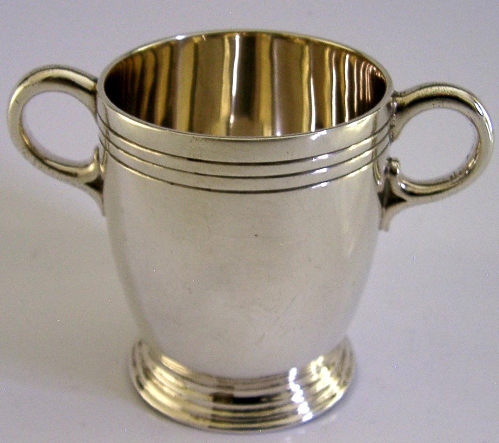 An Art Deco sterling silver twin-handled cup featuring horizontal incised line detailing, loop handles, a flared foot, and a gilt interior. View II