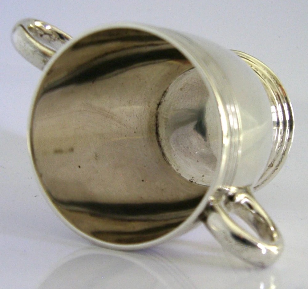 An Art Deco sterling silver twin-handled cup featuring horizontal incised line detailing, loop handles, a flared foot, and a gilt interior. View IV