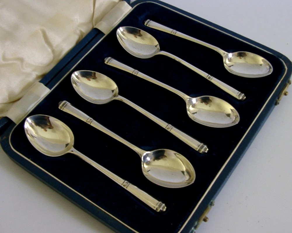 A set of six Art Deco sterling silver teaspoons arranged neatly inside a dark blue velvet-lined presentation case. View II