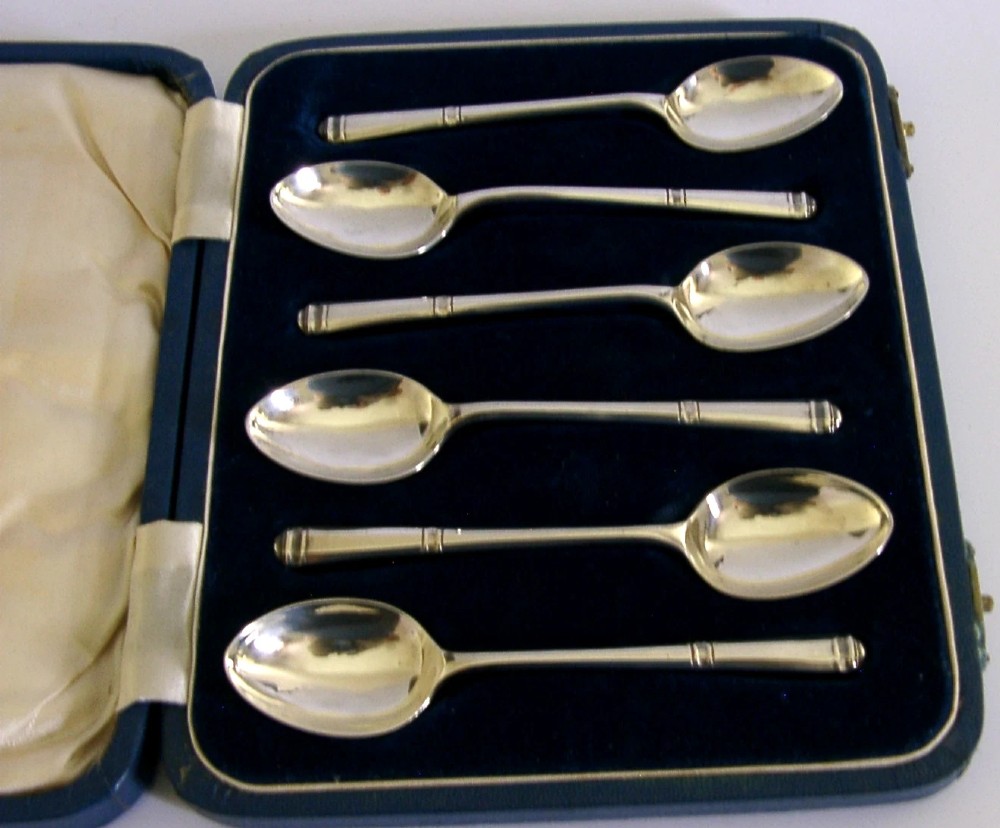 A set of six Art Deco sterling silver teaspoons arranged neatly inside a dark blue velvet-lined presentation case. View III