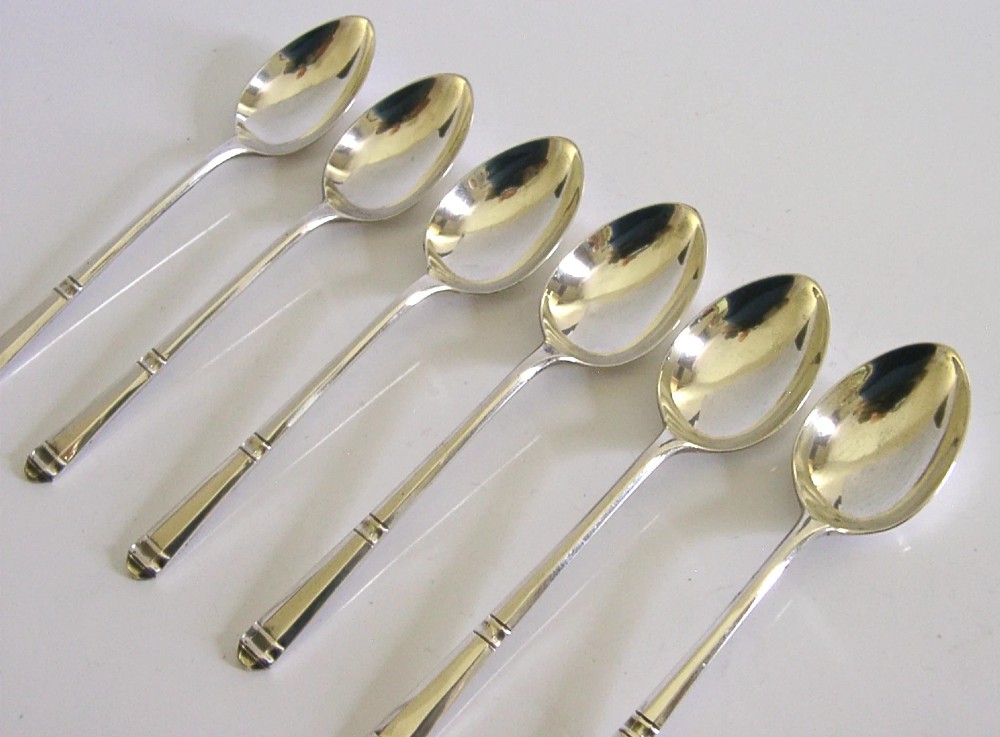 A set of six Art Deco sterling silver teaspoons arranged neatly inside a dark blue velvet-lined presentation case. View V