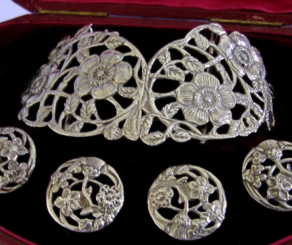 An Edwardian sterling silver belt buckle and four matching round buttons with pierced English rose motifs, presented inside a crimson velvet-lined oval case. View II