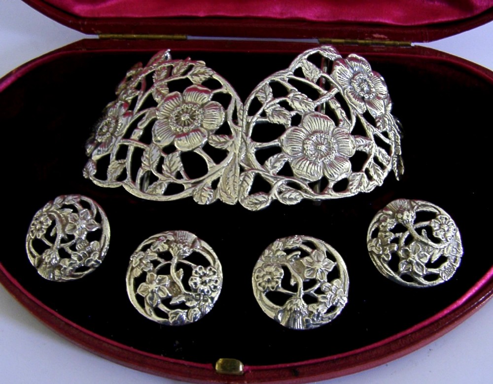 An Edwardian sterling silver belt buckle and four matching round buttons with pierced English rose motifs, presented inside a crimson velvet-lined oval case. View III