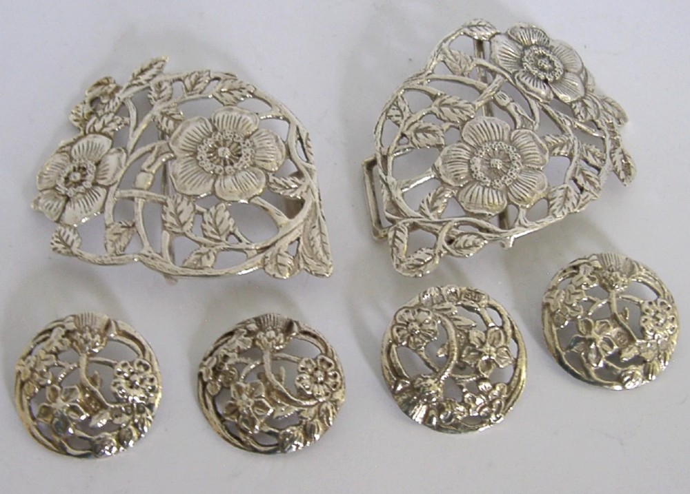 An Edwardian sterling silver belt buckle and four matching round buttons with pierced English rose motifs, presented inside a crimson velvet-lined oval case. View V