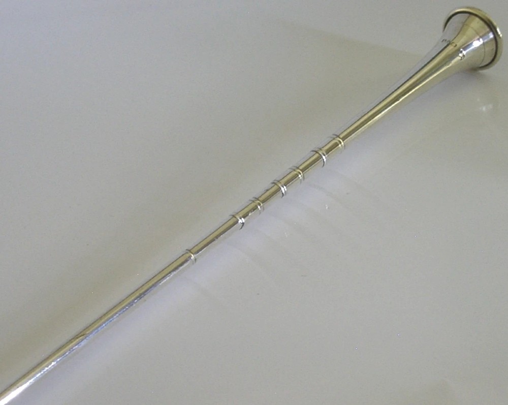 An Edwardian sterling silver hunting horn with ribbed body accents and a flared bell resting on a pale surface. View III