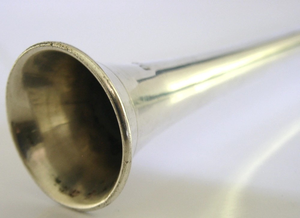 An Edwardian sterling silver hunting horn with ribbed body accents and a flared bell resting on a pale surface. View V