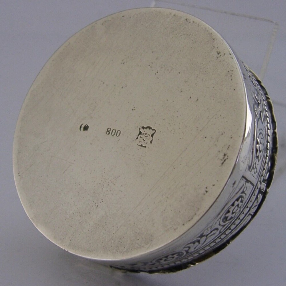 A circular antique silver trinket box featuring embossed relief depicting putti playing beneath floral garlands. View IX
