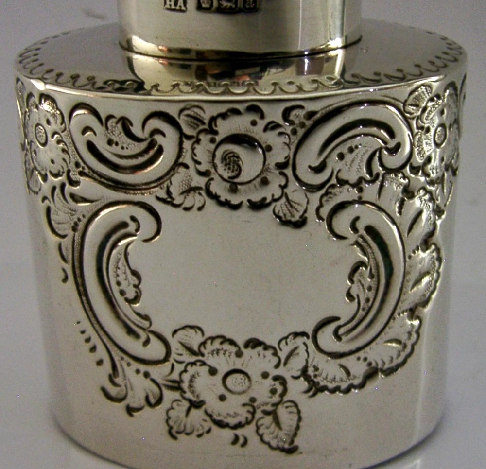 A cylindrical Victorian sterling silver tea caddy featuring chased floral and scroll motifs with a fitted cylindrical lid displaying hallmarks. View II