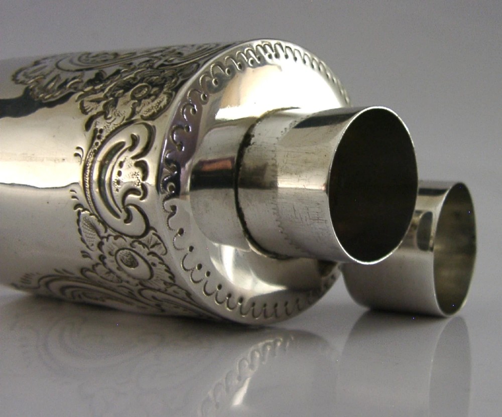 A cylindrical Victorian sterling silver tea caddy featuring chased floral and scroll motifs with a fitted cylindrical lid displaying hallmarks. View V