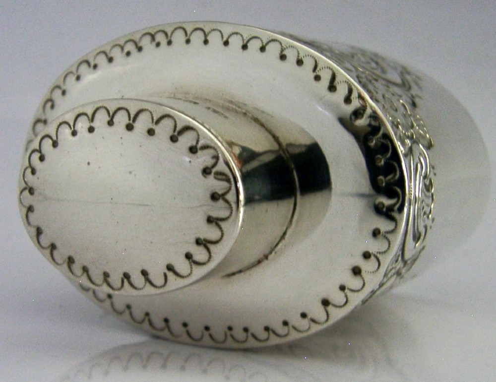 A cylindrical Victorian sterling silver tea caddy featuring chased floral and scroll motifs with a fitted cylindrical lid displaying hallmarks. View VII