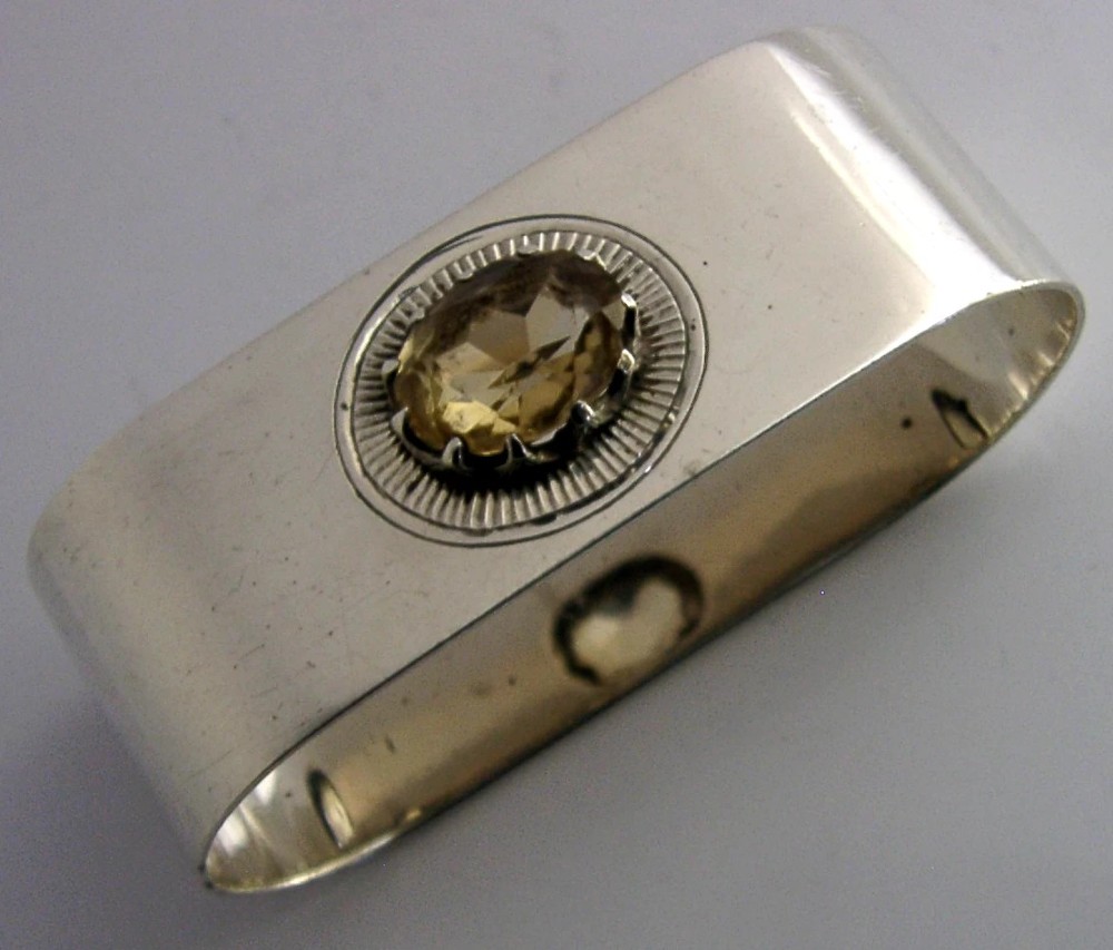 A polished rectangular sterling silver napkin ring set with a central oval citrine gemstone within a sunburst engraved surround.