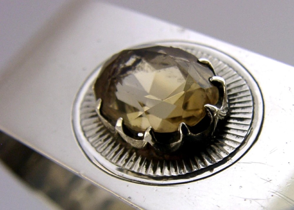 A polished rectangular sterling silver napkin ring set with a central oval citrine gemstone within a sunburst engraved surround. View II