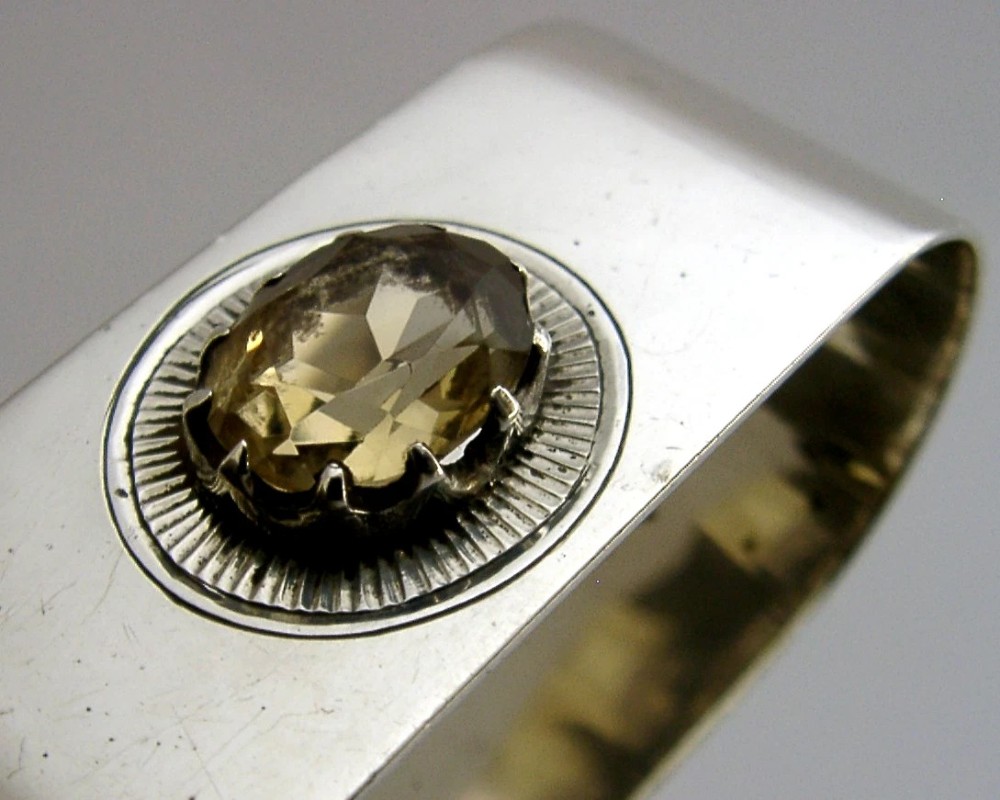 A polished rectangular sterling silver napkin ring set with a central oval citrine gemstone within a sunburst engraved surround. View III
