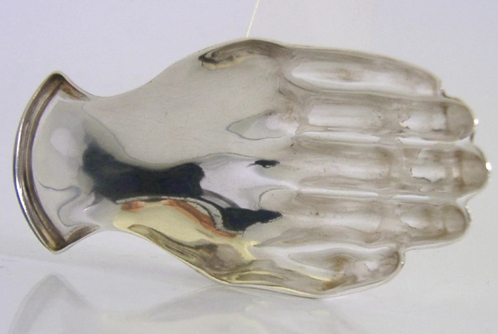 A sterling silver tea caddy spoon shaped like an open human hand with visible hallmarks stamped near the wrist handle. View IV