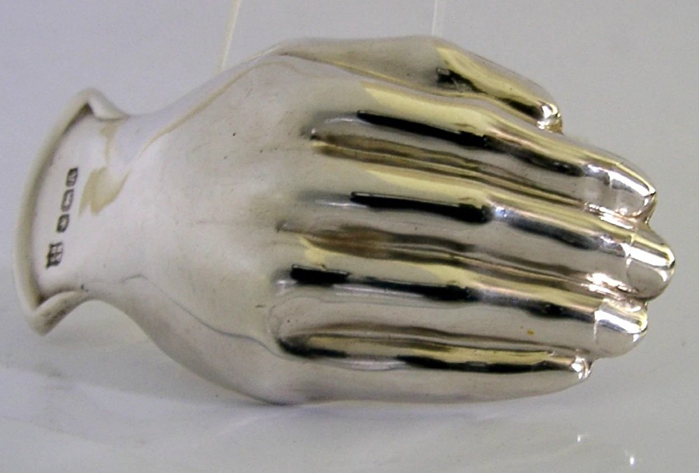 A sterling silver tea caddy spoon shaped like an open human hand with visible hallmarks stamped near the wrist handle. View VI