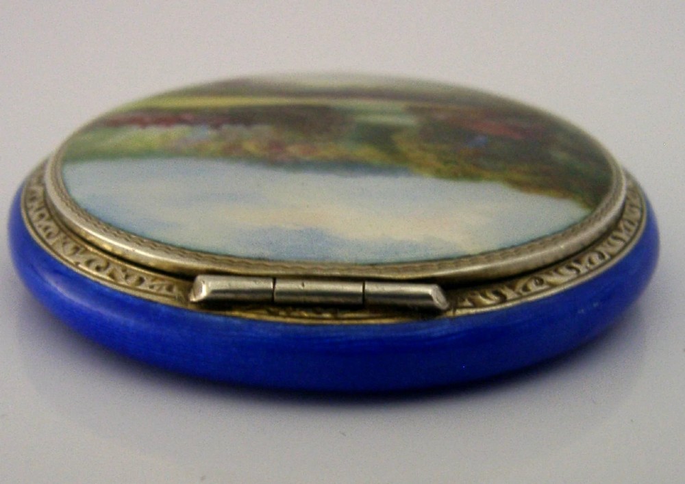 An open Art Deco sterling silver powder compact featuring a cobalt blue enamel rim and a hand-painted landscape scene on the lid interior. View X