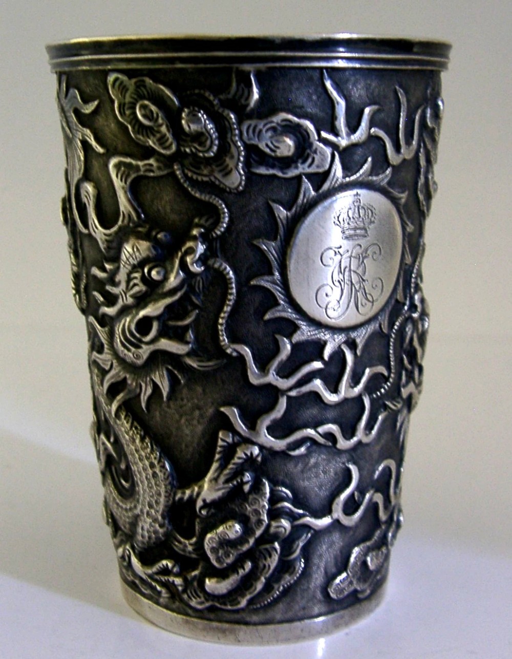A cylindrical Chinese export silver beaker featuring high-relief repousse dragon motifs and an oval cartouche engraved with a royal monogram beneath a crown.