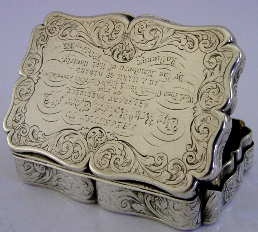 An engraved Victorian sterling silver snuff box with shaped edges, scrollwork border, and engraved inscription on the lid.