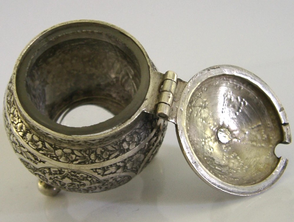 An antique hand-engraved solid silver mustard pot featuring arabesque foliage patterns, a hinged lid with finial, a spoon aperture, and three ball feet. View VII