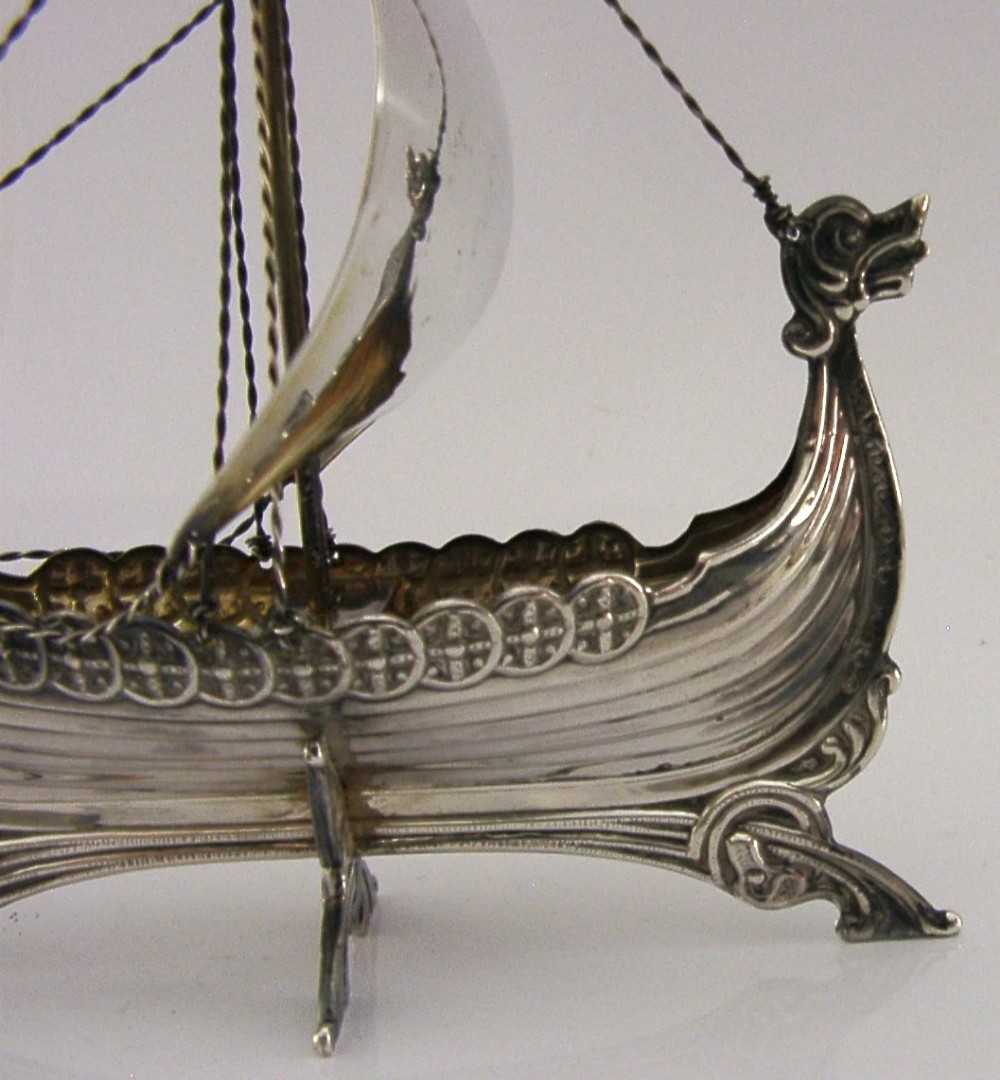 A detailed solid silver model of a Viking longship featuring a dragon head prow, raised sail, pennant flag, and miniature shields along the gunwale. View II