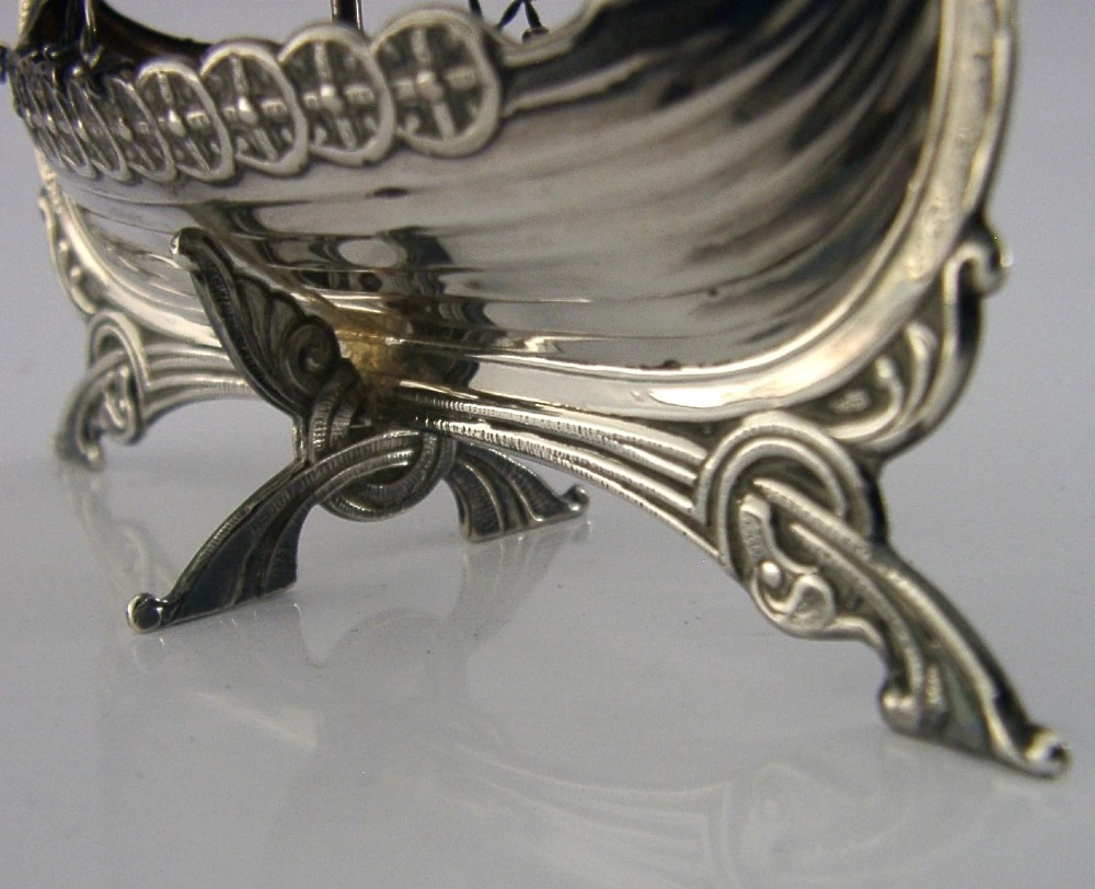 A detailed solid silver model of a Viking longship featuring a dragon head prow, raised sail, pennant flag, and miniature shields along the gunwale. View V