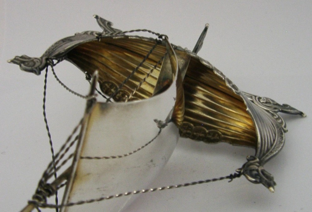 A detailed solid silver model of a Viking longship featuring a dragon head prow, raised sail, pennant flag, and miniature shields along the gunwale. View XI
