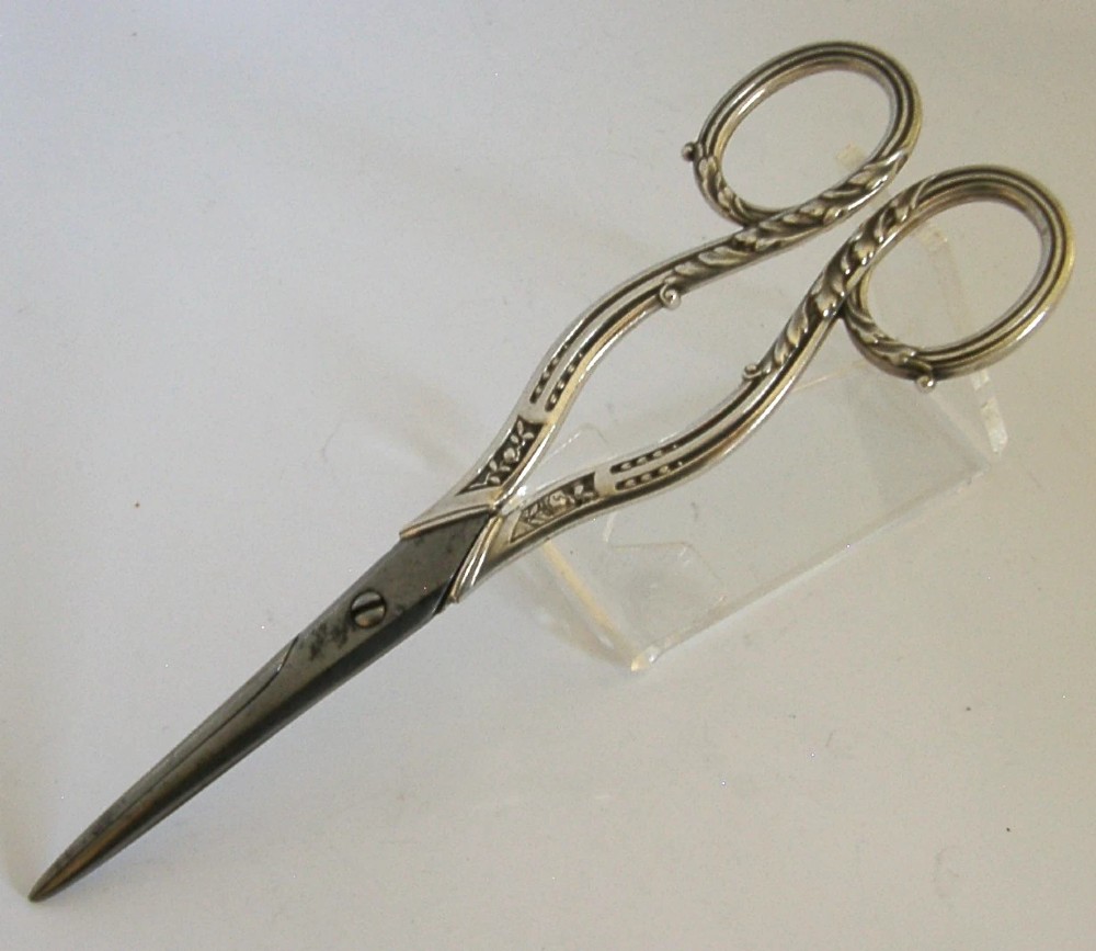 Antique French scissors featuring ornate sterling silver handles decorated with relief foliage motifs and tapered steel blades.
