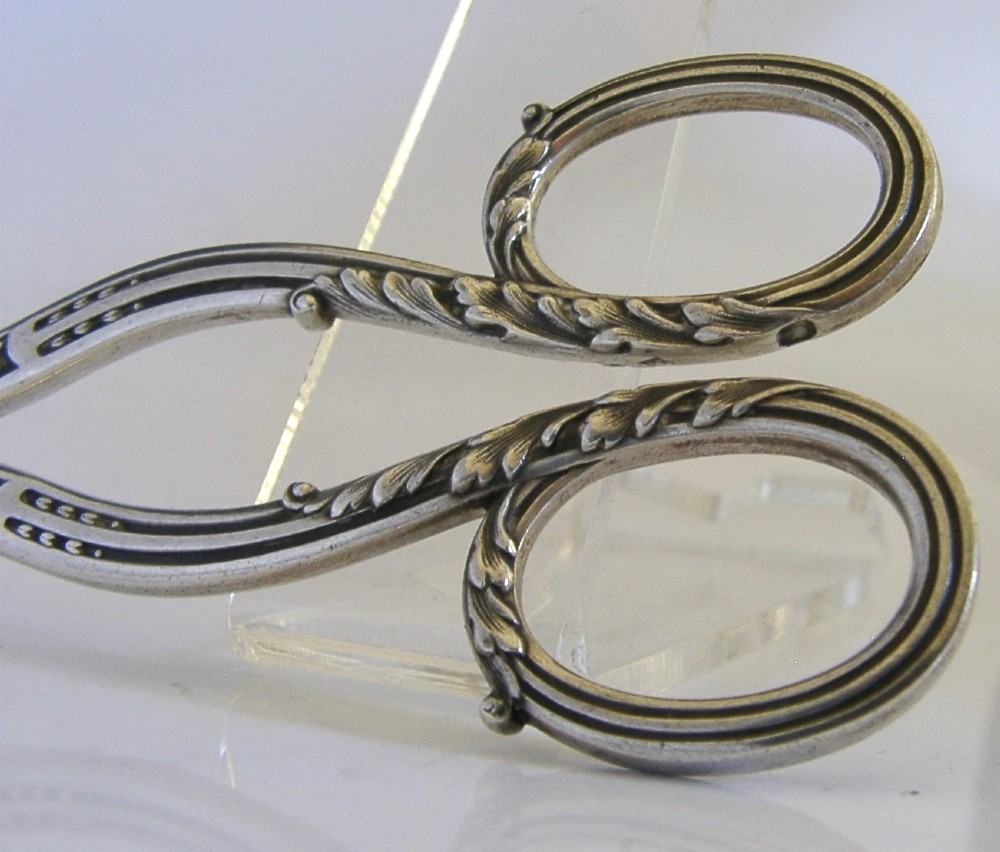 Antique French scissors featuring ornate sterling silver handles decorated with relief foliage motifs and tapered steel blades. View II