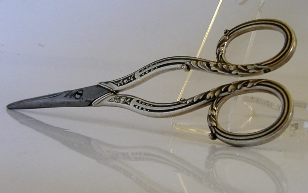 Antique French scissors featuring ornate sterling silver handles decorated with relief foliage motifs and tapered steel blades. View V