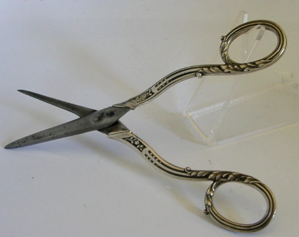 Antique French scissors featuring ornate sterling silver handles decorated with relief foliage motifs and tapered steel blades. View VI