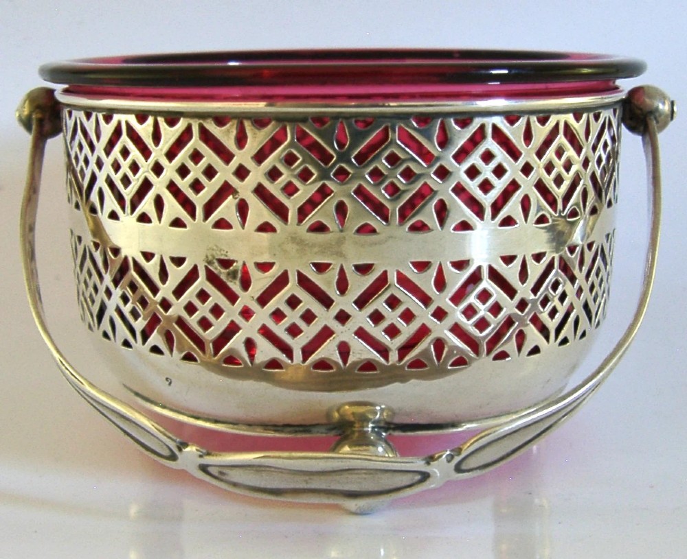 An Edwardian sterling silver pierced basket featuring a lattice geometric pattern, a swing handle, and a fitted cranberry red glass liner. View IV