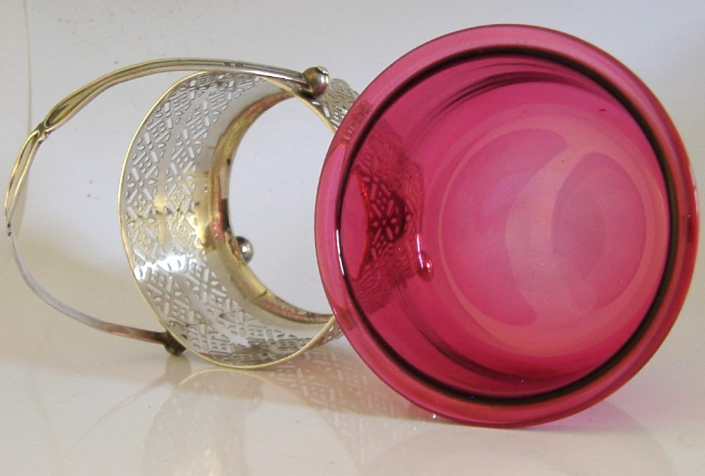 An Edwardian sterling silver pierced basket featuring a lattice geometric pattern, a swing handle, and a fitted cranberry red glass liner. View VI