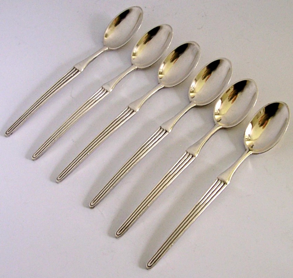 A set of six mid-century solid silver spoons featuring slim handles with reeded linear decoration and oval bowls.