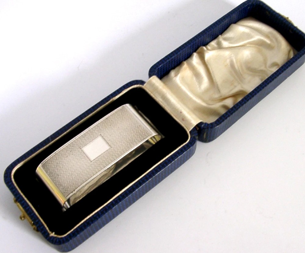 An Art Deco sterling silver napkin ring featuring engine-turned geometric engraving, displayed inside an open blue silk and velvet-lined fitted case.