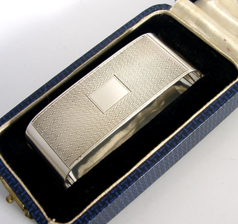 An Art Deco sterling silver napkin ring featuring engine-turned geometric engraving, displayed inside an open blue silk and velvet-lined fitted case. View III