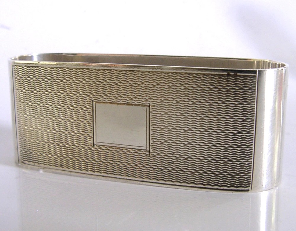 An Art Deco sterling silver napkin ring featuring engine-turned geometric engraving, displayed inside an open blue silk and velvet-lined fitted case. View IV