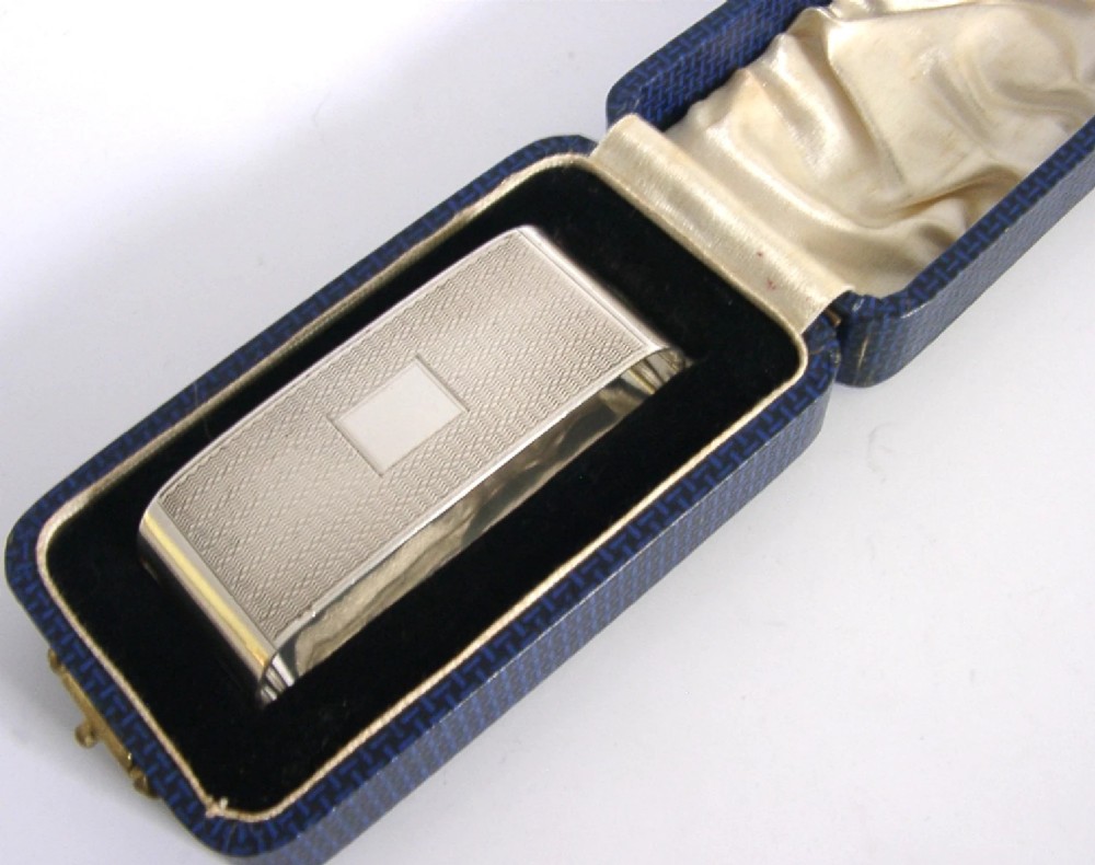 An Art Deco sterling silver napkin ring featuring engine-turned geometric engraving, displayed inside an open blue silk and velvet-lined fitted case. View V