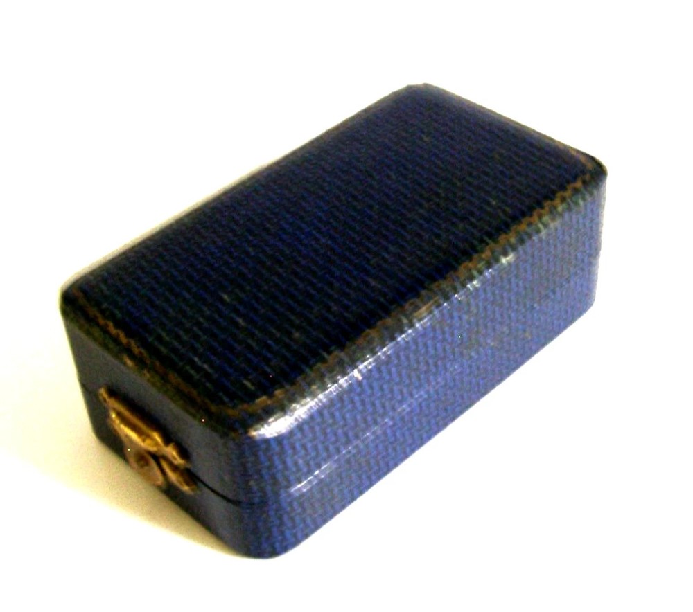 An Art Deco sterling silver napkin ring featuring engine-turned geometric engraving, displayed inside an open blue silk and velvet-lined fitted case. View VIII